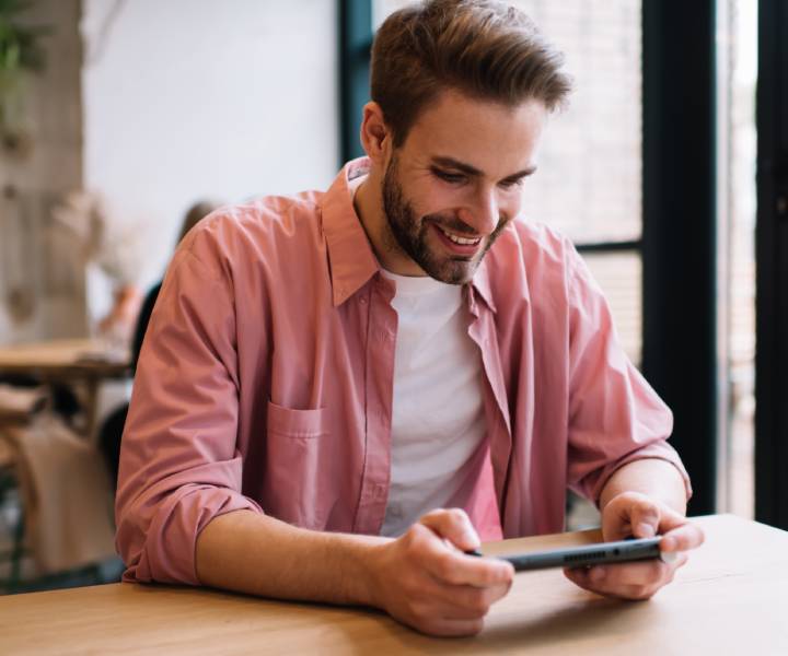 Man smiling while playing a Nintendo Switch console during the day in a public cafe. 