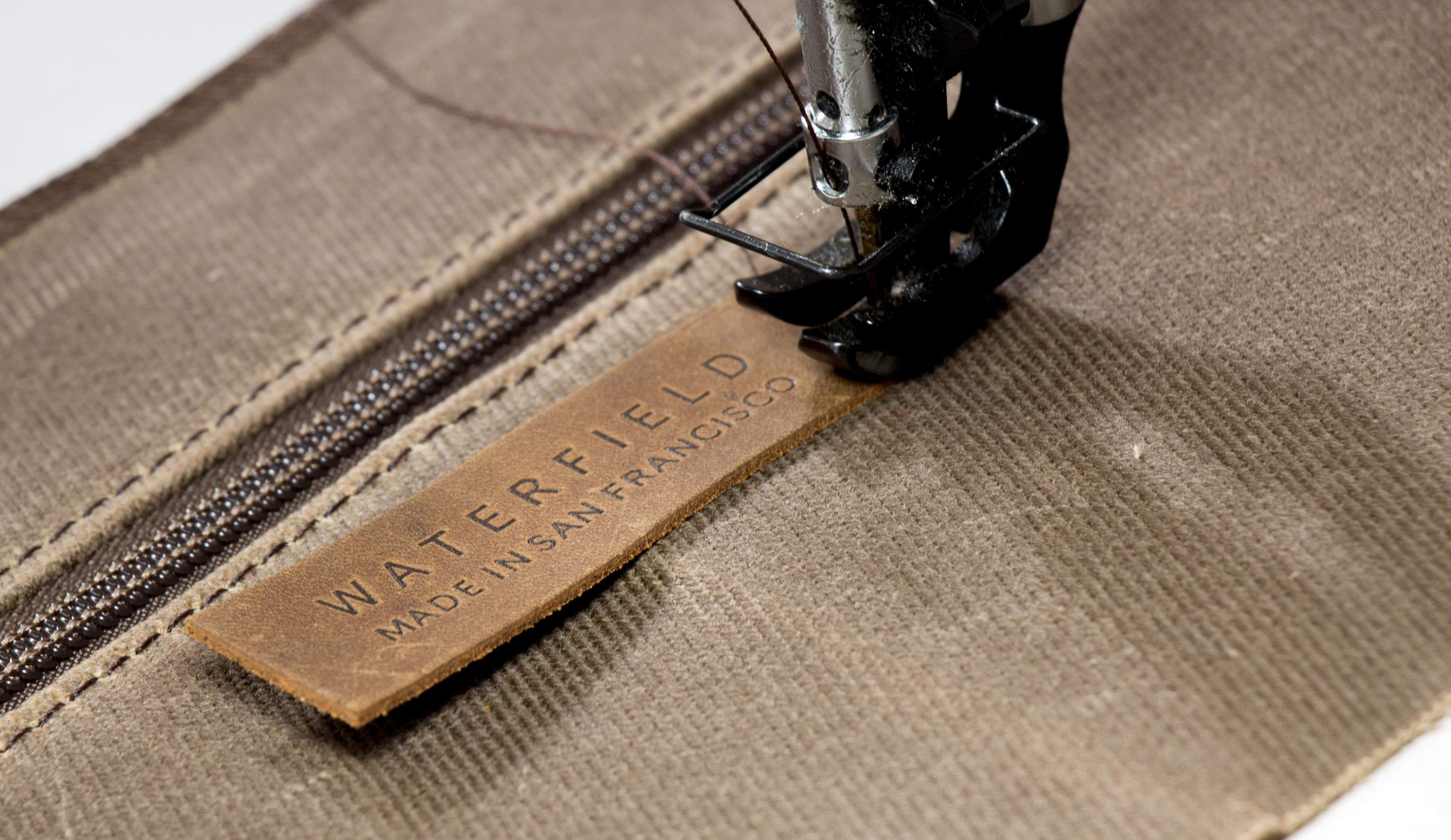 Close-up of industrial sewing machine stitching brown fabric with WaterField label