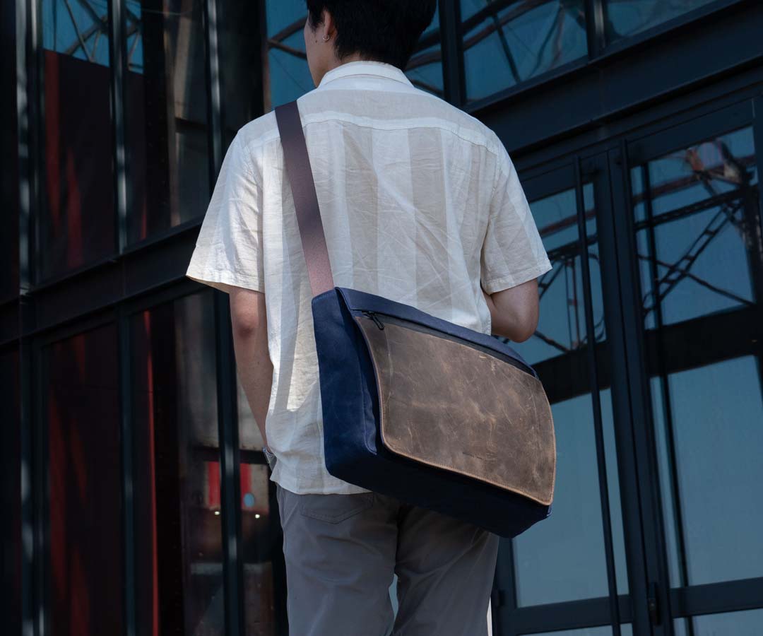 Person wearing crossbody messenger bag in brown leather while walking outdoors