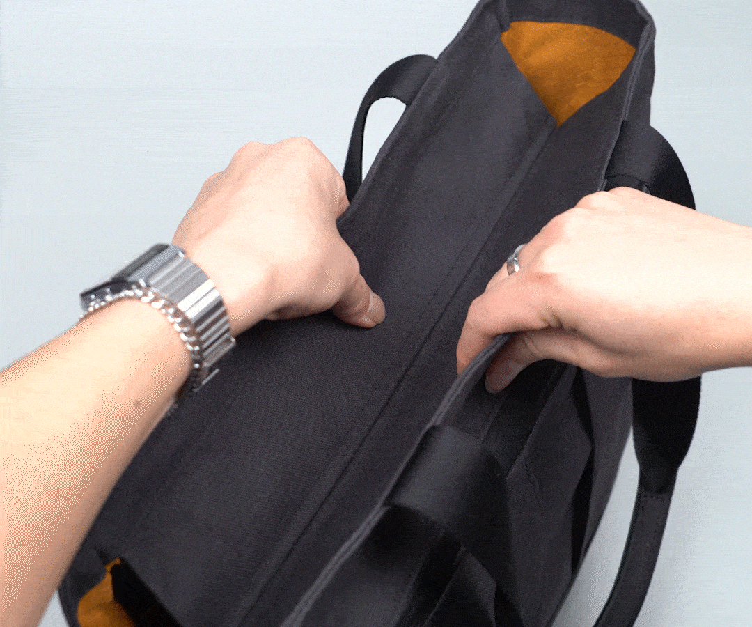 Hands opening the Shinjuku Tote bag, showing its yellow interior and magnetic closure